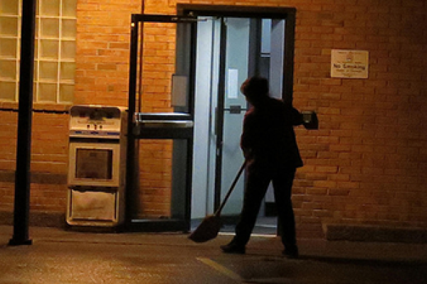 Environmental services staff member sweeping outside in front of building doorway