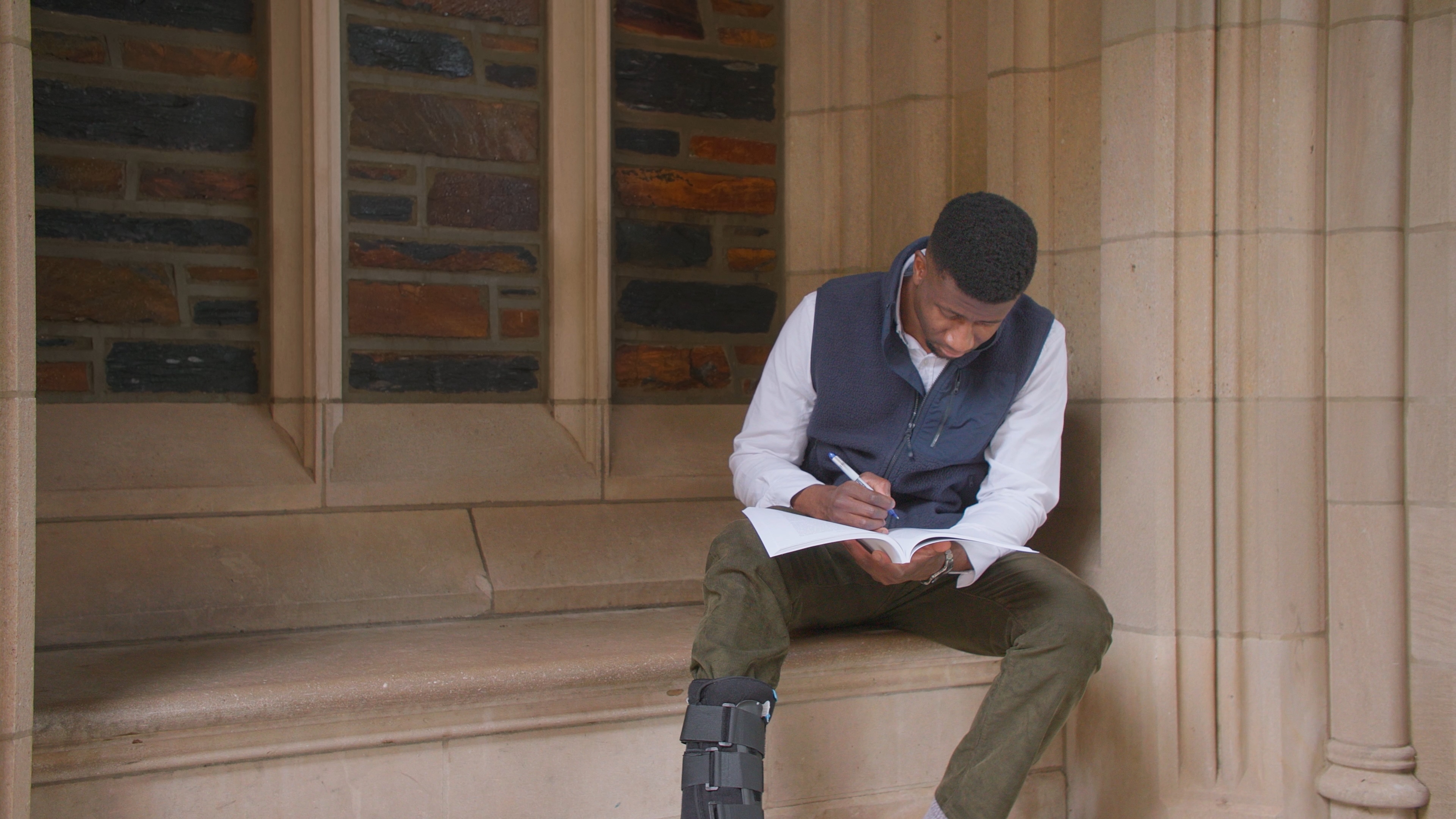 Image of a student or resident reading, sitting by Duke marble/stone building