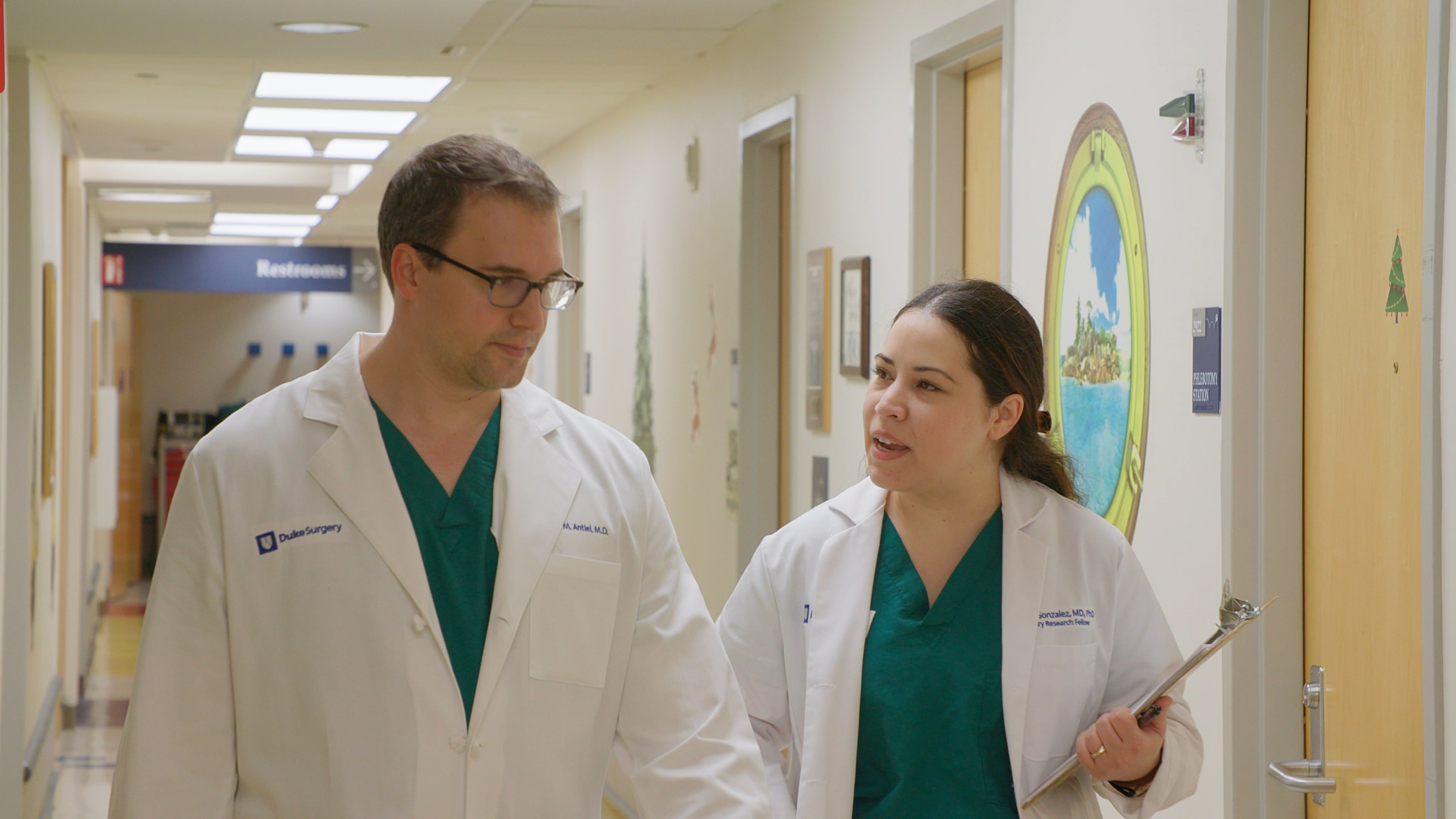 Dr. Ryan Antiel walking down a clinical hallway with a resident, both in white coats