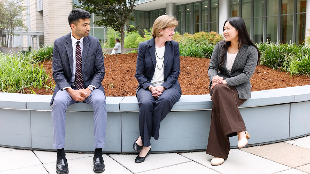 Dean Klotman interviewing two students while sitting outside on a planter bed. 