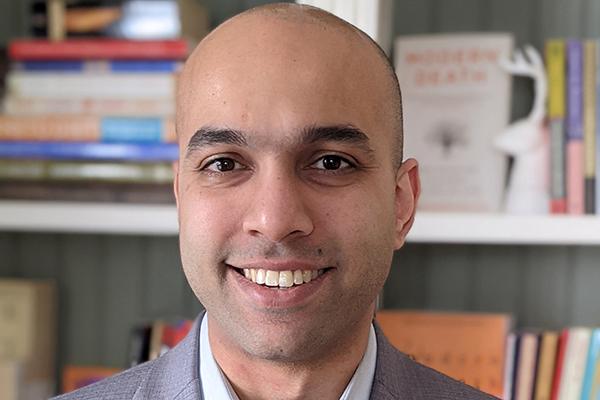 Headshot Haider Warraich smiling, in front ot book shelves