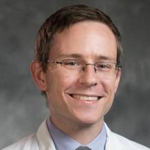 Joshua Briscoe headshot, smiling in white coat